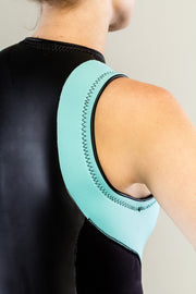 A slender woman is standing in a sleeveless shorty Truli-Mi wetsuit by Truli Wetsuits for women. The trim is light blue and the rest of the wetsuit is black. The view is from the back as a close up of the sleeveless shoulder.